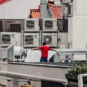 Man standing in front of several AC Units that need to be serviced on a hot summer day
