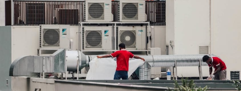 Man standing in front of several AC Units that need to be serviced on a hot summer day